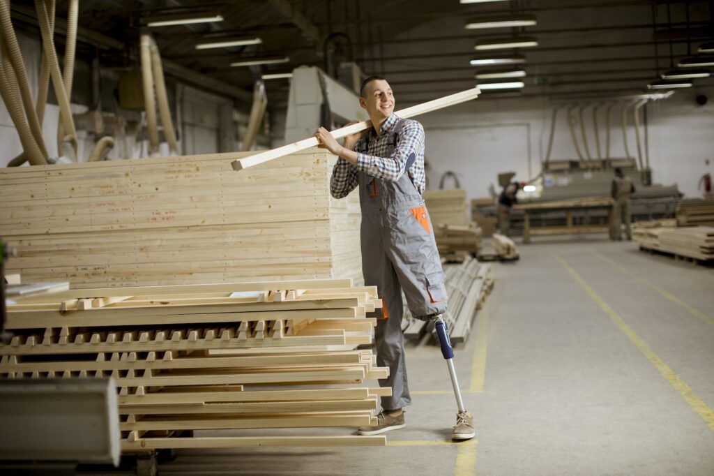 Disabled young man with an artificial leg is working at furniture factory